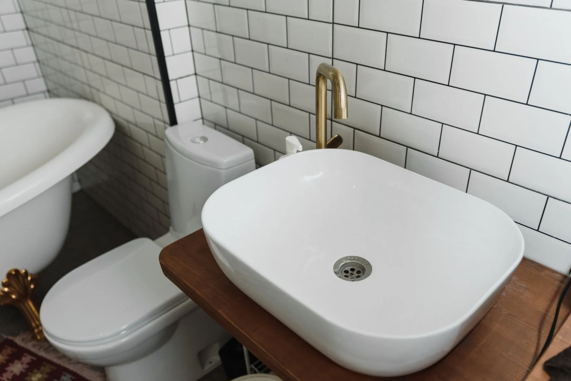 A bathroom with a brass faucet, vessel sink, toilet, and tub