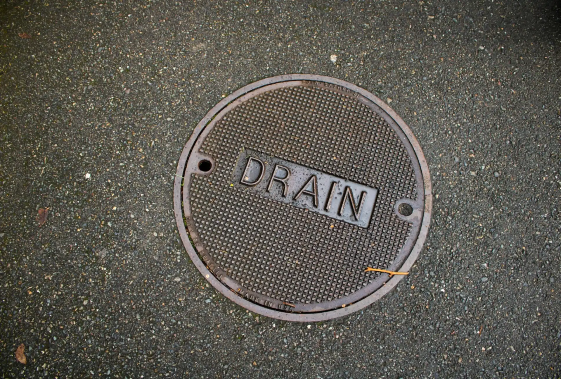 A round metal drain cover stamped “DRAIN” set in asphalt