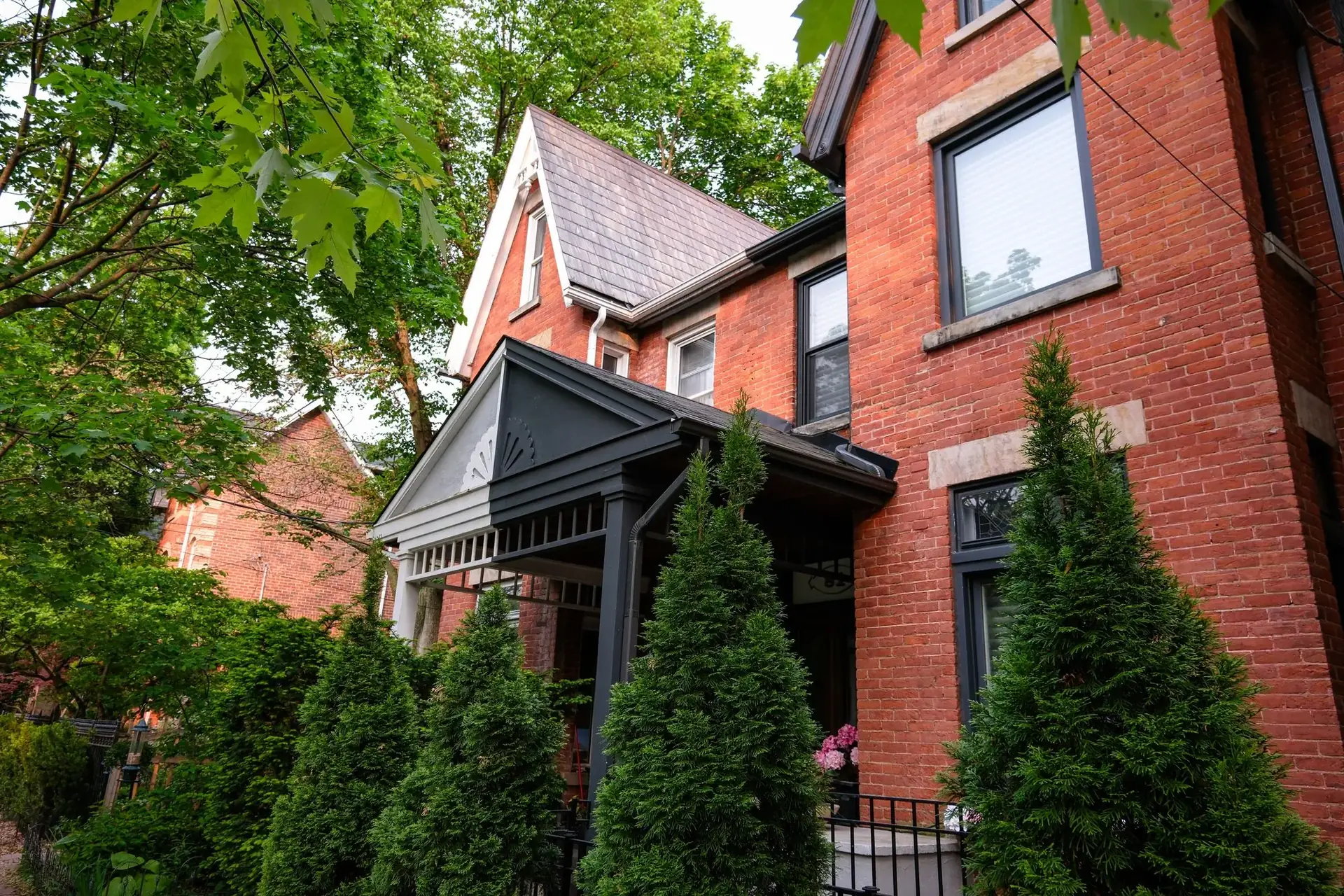 A red-brick Toronto house surrounded by evergreens